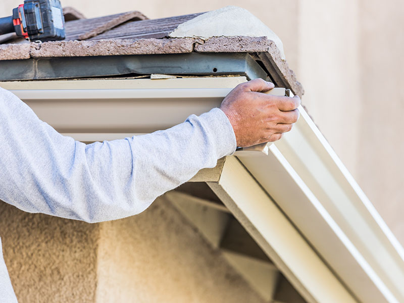 Close-up of a worker's hand installing aluminum gutters to the fascia part of a residential home